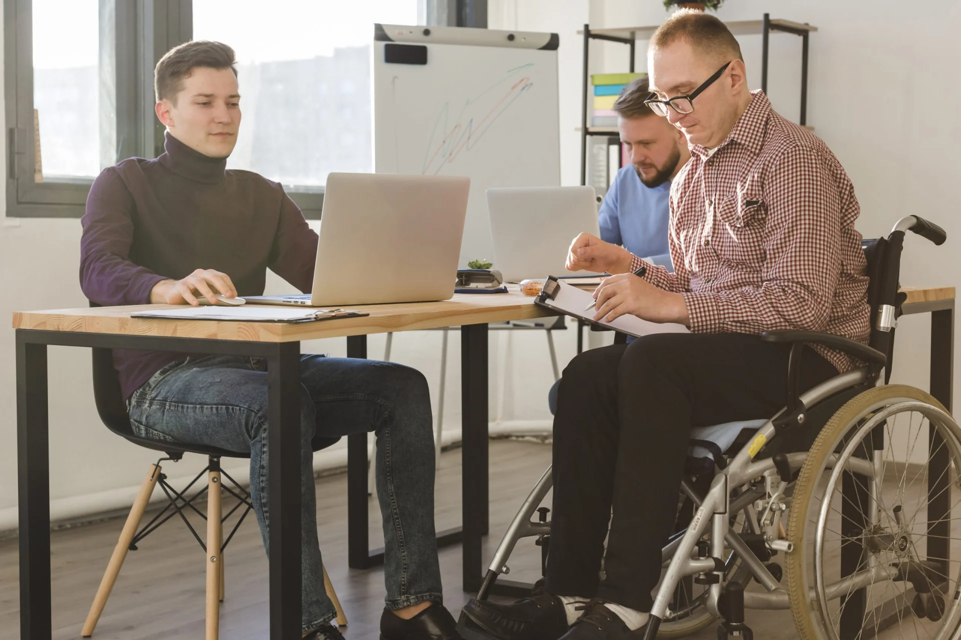 Colleagues celebrating teamwork in an inclusive office environment, with a wheelchair user high-fiving coworkers during a collaborative moment