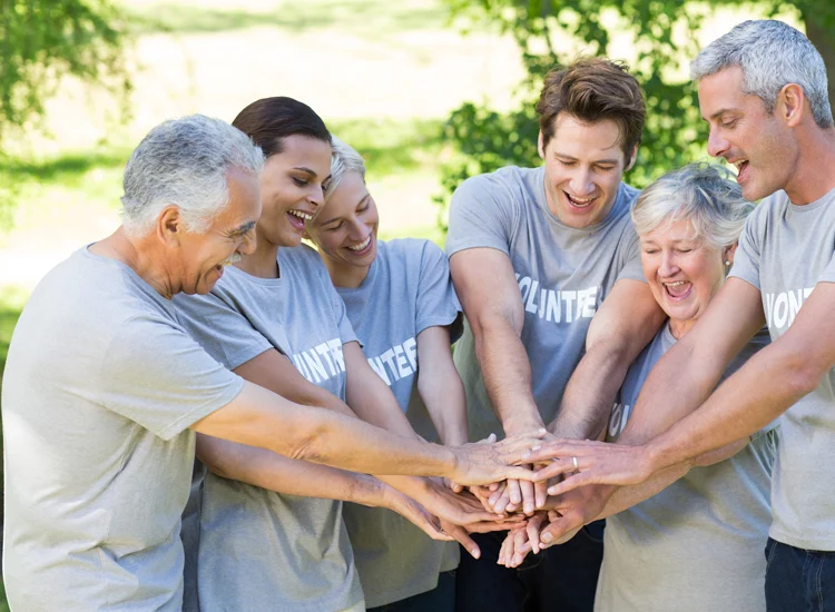 Volunteers standing together outdoors with hands stacked in a show of teamwork, inclusion, and community support