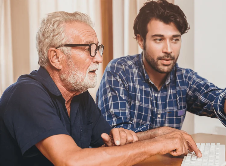 Support professional assisting an older adult with computer use, demonstrating digital skills and personalized guidance