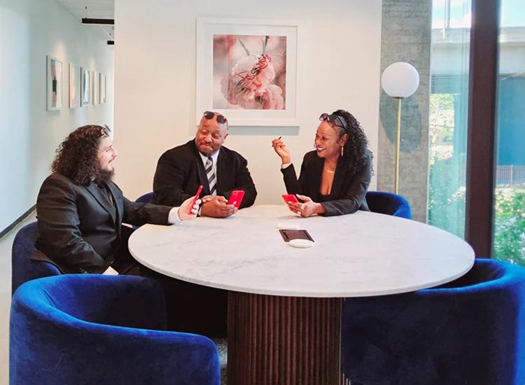 Vista Supports team members engaged in a collaborative discussion around a table, reviewing information on mobile devices in a modern office setting