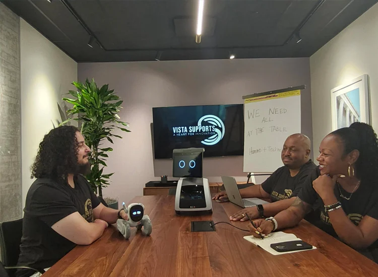 Vista Supports team members collaborating around a conference table with assistive technology and a service robot during a planning meeting
